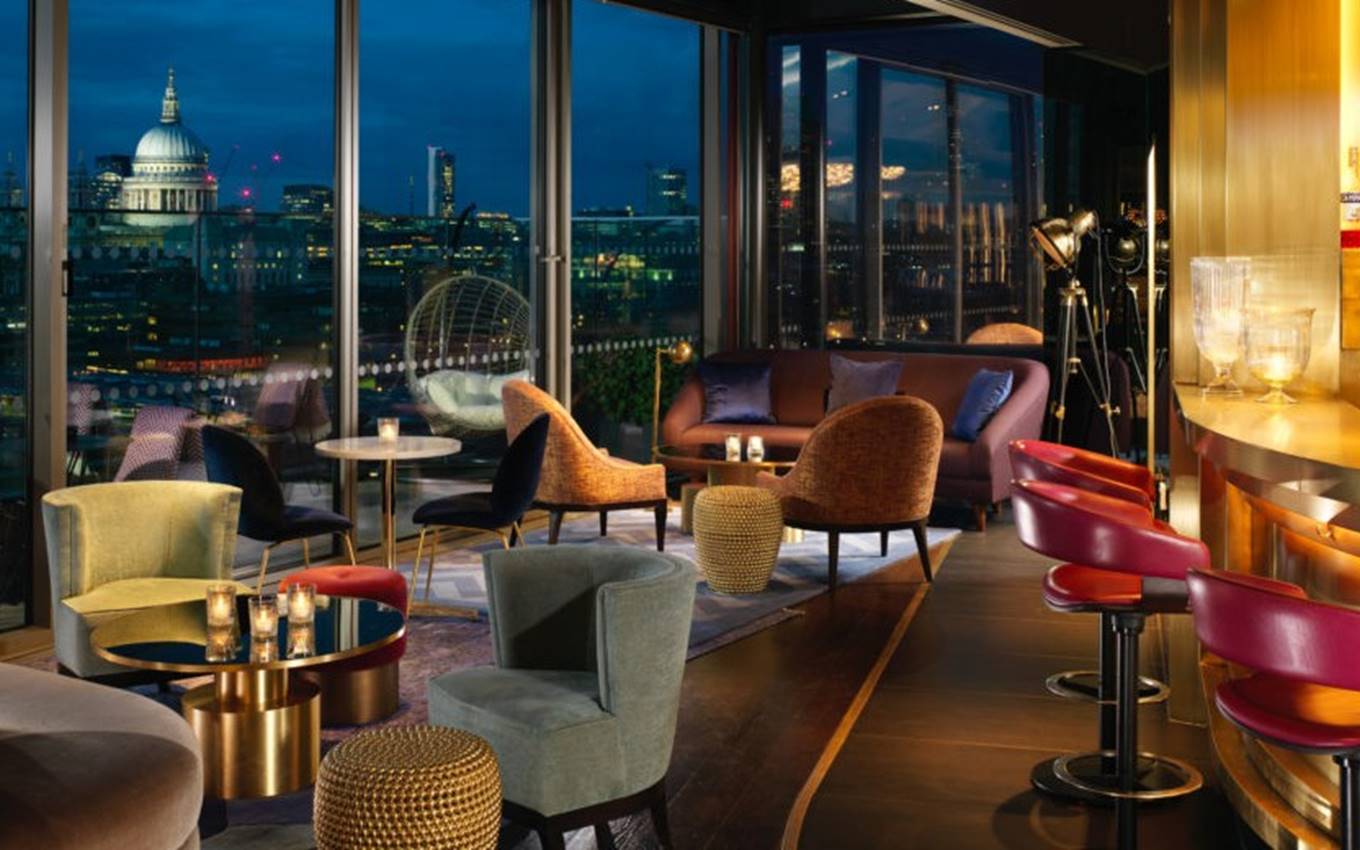 A chic rooftop lounge in London with vibrant seating and large windows showcasing a view of St. Paul’s Cathedral at night.