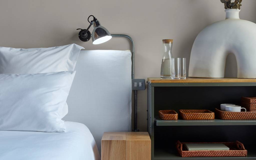A neatly made bed with white sheets and a decorative vase placed on a night stand, creating a serene and inviting atmosphere.