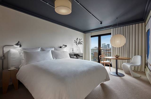 Modern hotel bedroom at One Hundred Shoreditch with a white bed, small table and a balcony view of the London skyline.