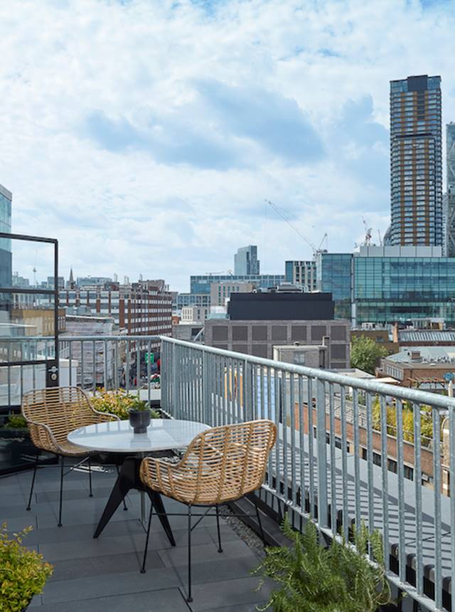 Rooftop balcony with rattan chairs and table, with London skyline views on a clear day, showing a relaxing urban retreat.