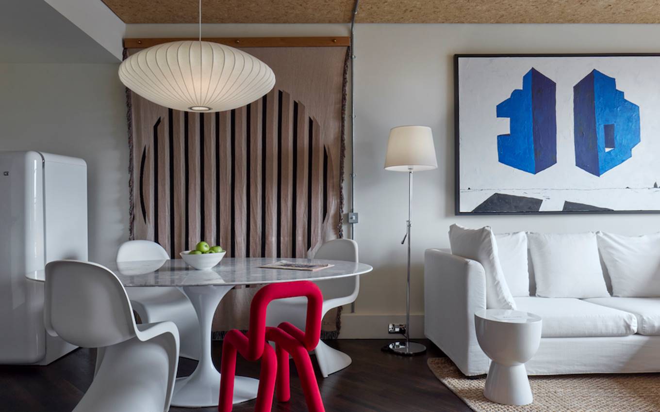 Dining nook with white table, modern chairs, vibrant red chair, white lamp and bold blue artwork at One Hundred Shoreditch.