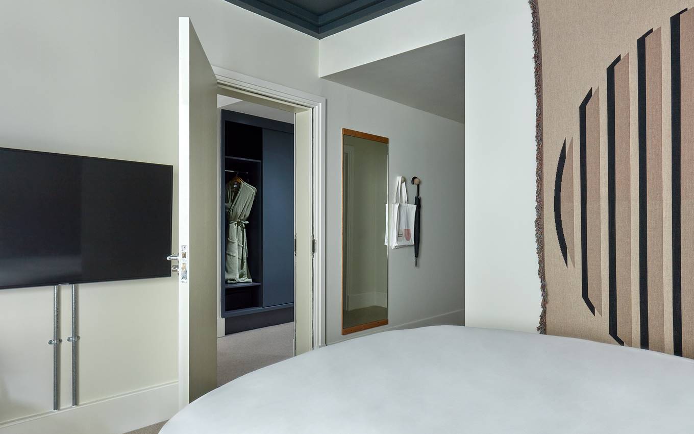 Bedroom at One Hundred Shoreditch with a striped tapestry, adjacent to an open closet displaying a robe.