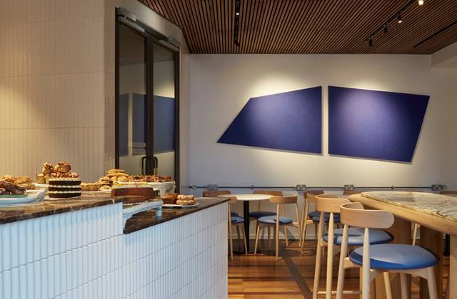Café with marble tables, blue chairs, and a pastry counter with various desserts on display at One Hundred Shoreditch hotel.