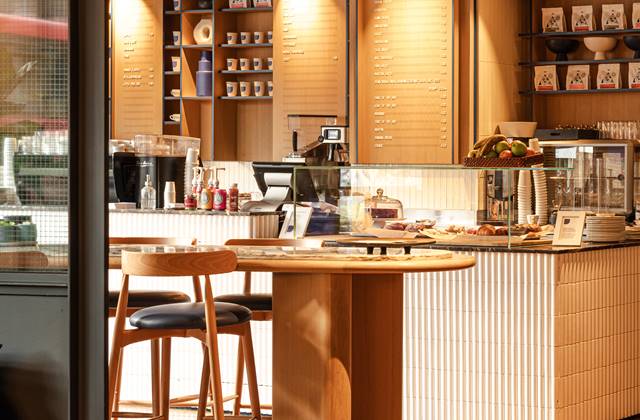 Coffee shop counter with light wood decor, a variety of coffee options displayed, and a round table with high seating.