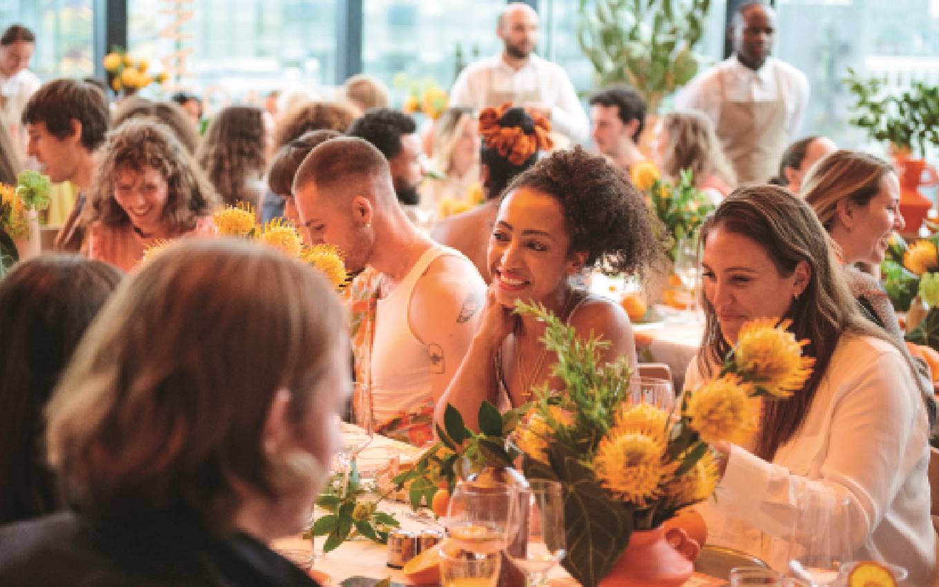 A gathering of individuals seated at tables adorned with vibrant sunflowers, enjoying a sunny day together.