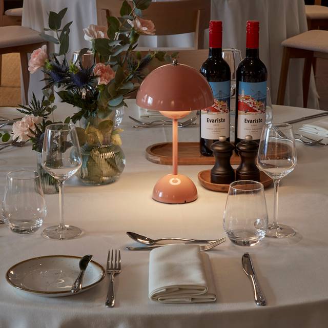 A table with wine bottles, flowers, and a pink lamp, creating a soft and inviting dining ambiance at One Hundred Shoreditch.