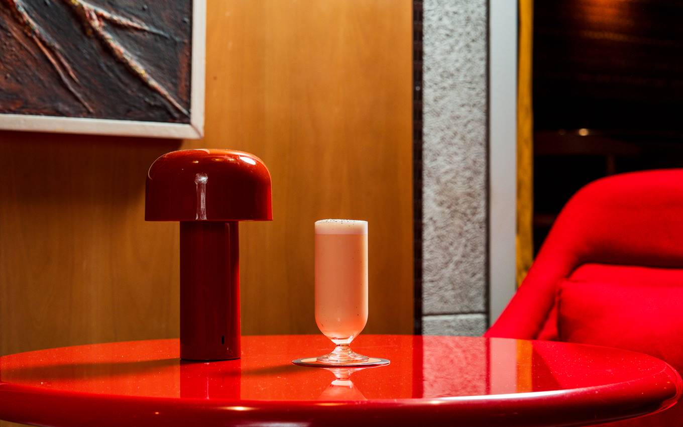 A red table with a mushroom-shaped lamp and a creamy cocktail in a sleek, modern setting at a London bar.