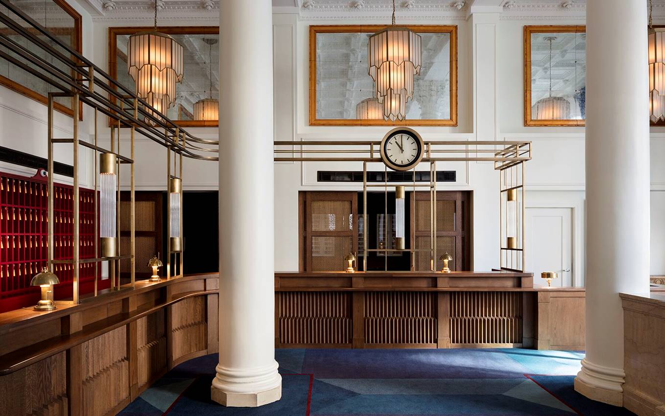 Classic hotel lobby at Riggs DC with wood and brass details, a clock, and art deco lighting, evoking timeless elegance.