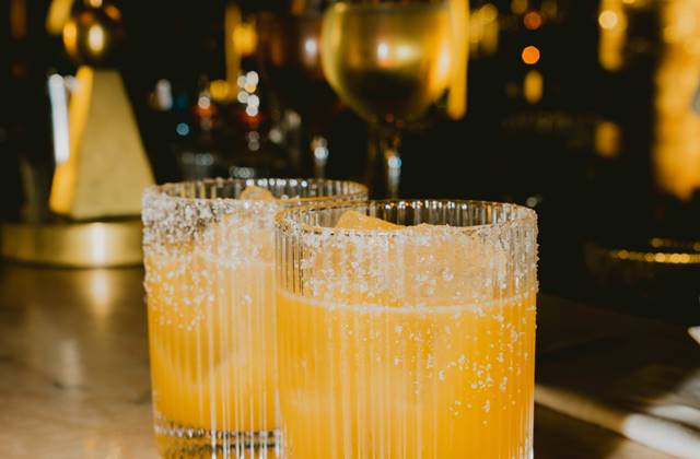 Two glasses of vibrant orange drink placed on a polished bar surface, inviting and refreshing in appearance.