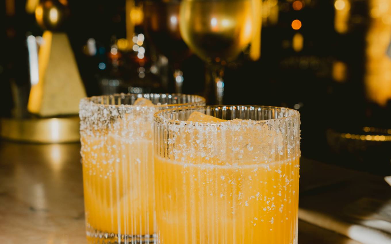 Two glasses of vibrant orange drink placed on a polished bar surface, inviting and refreshing in appearance.