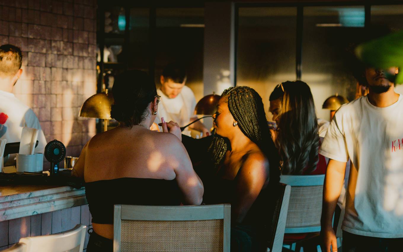 A lively bar scene featuring people socialising, with a woman seated on the bar, creating a vibrant atmosphere.