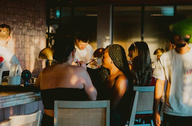 A lively bar scene featuring people socialising, with a woman seated on the bar, creating a vibrant atmosphere.