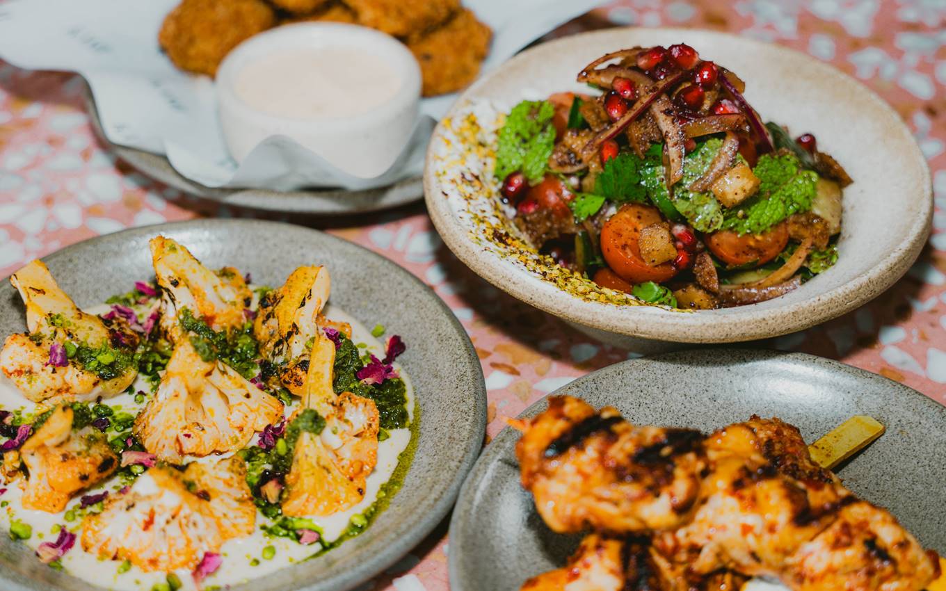 Vibrant Middle Eastern-inspired plates, including grilled cauliflower, salad with pomegranate, and skewered chicken.