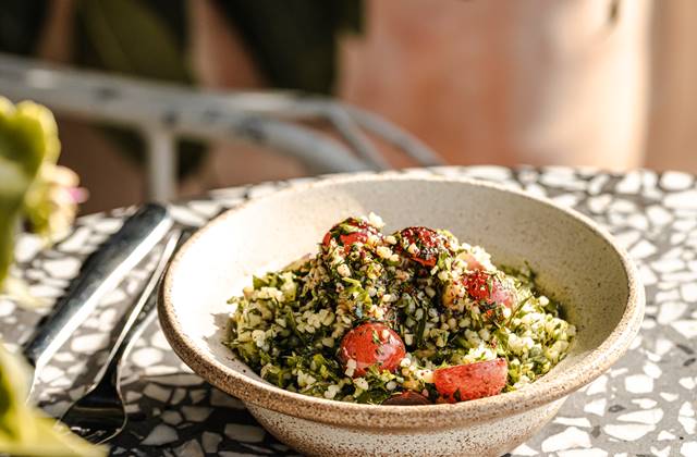 A bowl of tabbouleh with cherry tomatoes, parsley, and bulgur, on a terrazzo-patterned table in a London restaurant.