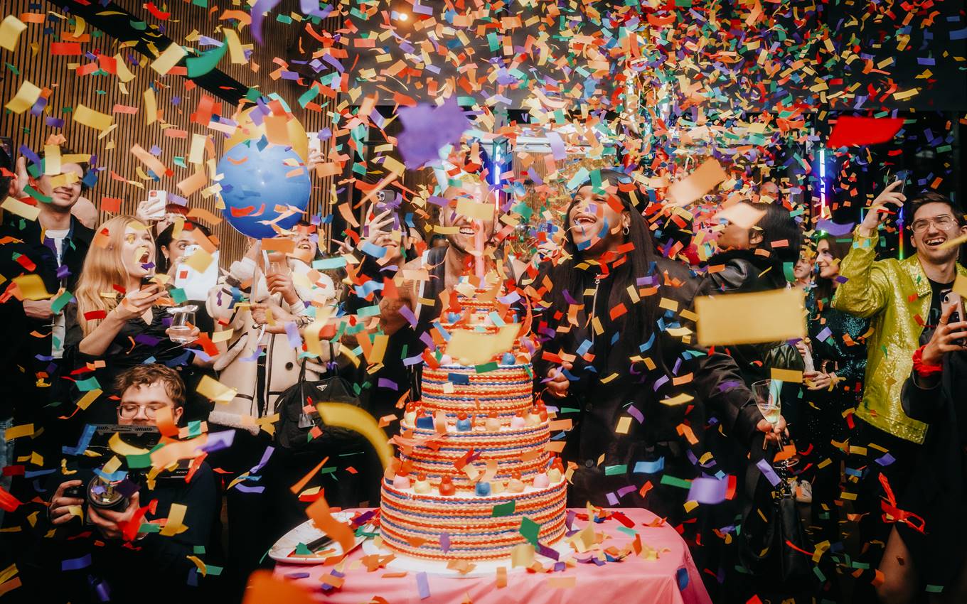 A joyful group of people celebrating a birthday party, surrounded by colourful confetti and festive decorations.