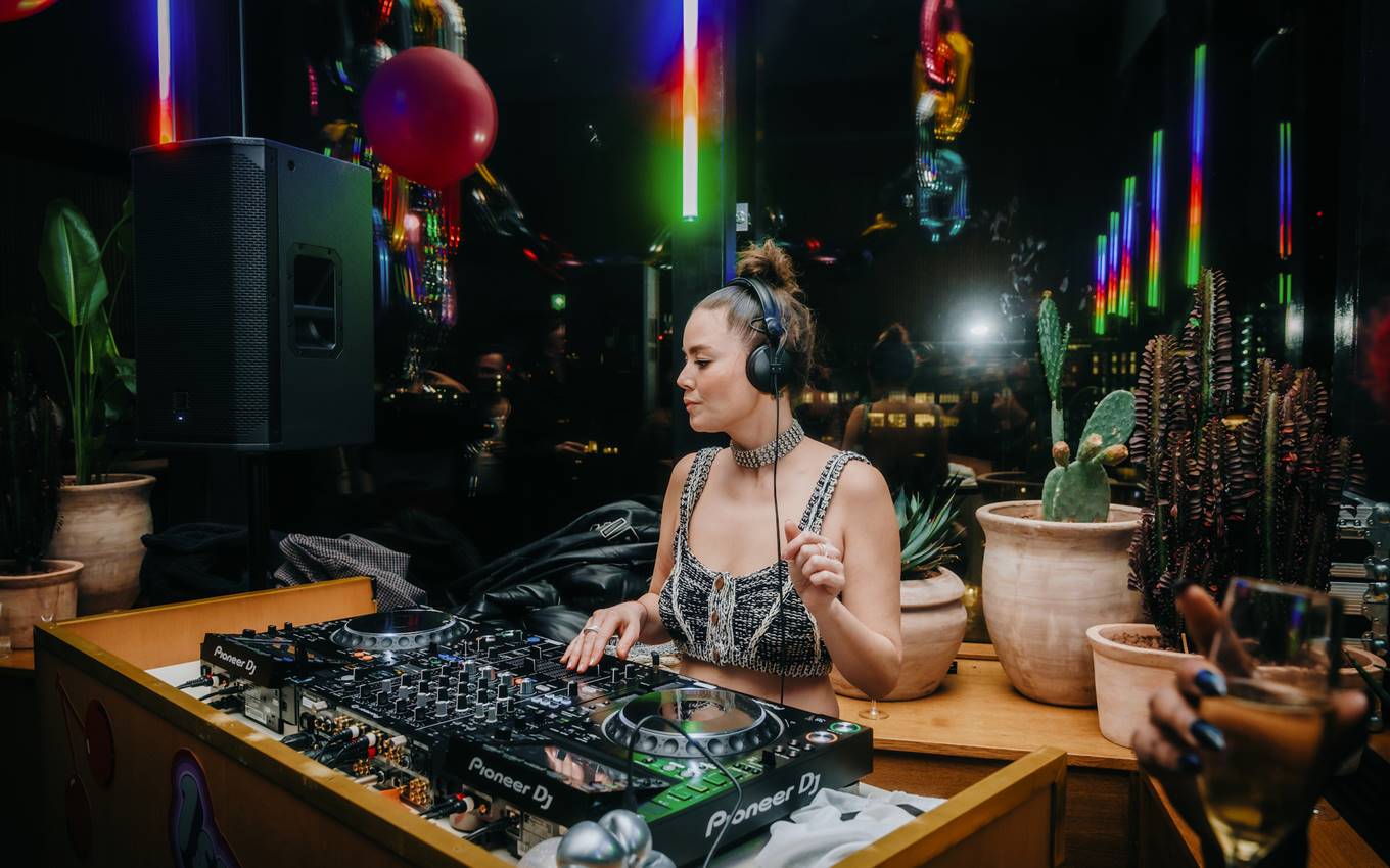 A DJ playing on a mixer, surrounded by neon lights and balloons, creating an upbeat atmosphere for a London party.