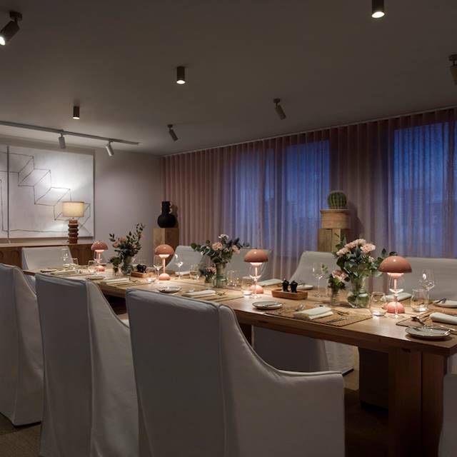 A private dining room in London with a long table, decorated with pink lamps, flowers, and modern art on the wall.