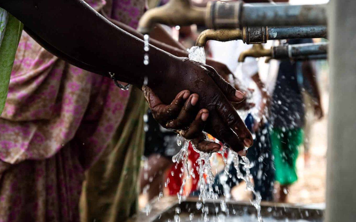 Hands under flowing water at an outdoor tap, symbolising access to clean water and hygiene practices.