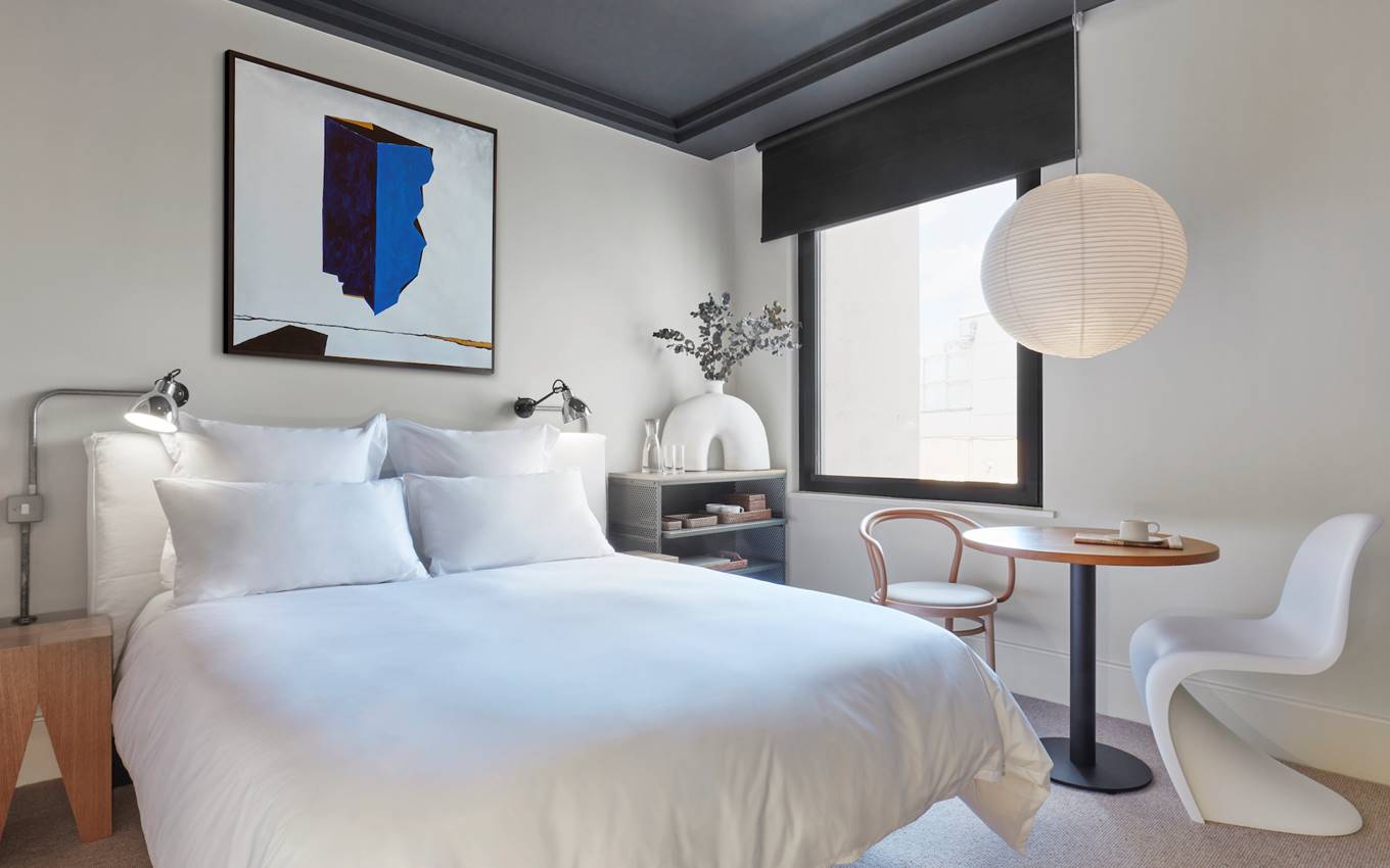 A serene bedroom featuring a white bed and an elegant painting adorning the wall, creating a tranquil atmosphere.