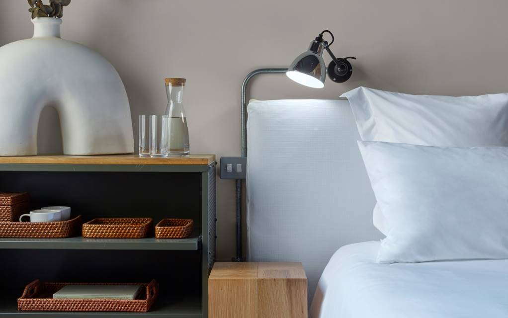 A neatly made bed with white sheets and a decorative vase placed on a table, creating a serene and inviting atmosphere.