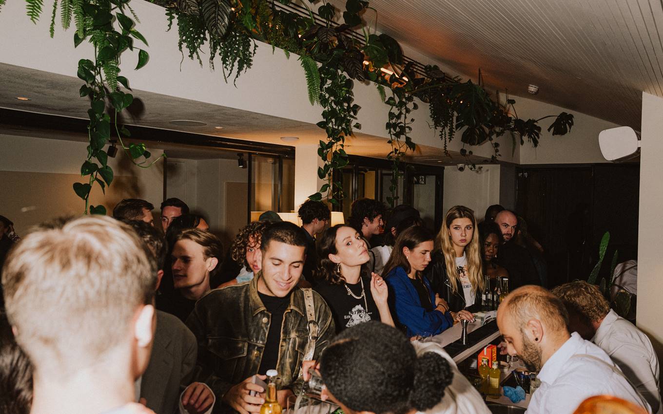 Crowd enjoying a lively London event indoor with greenery hanging from the ceiling, adding a natural element to the ambiance.