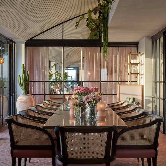 Elegant dining table with glass and woven chairs, floral centrepieces, and soft natural lighting in a London restaurant.
