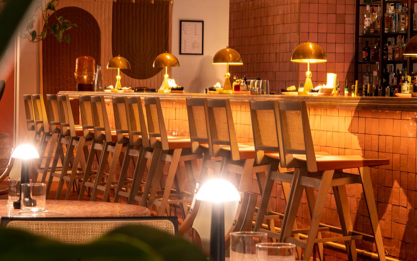A long wooden bar featuring stools and decorative lamps, creating a warm and inviting atmosphere.