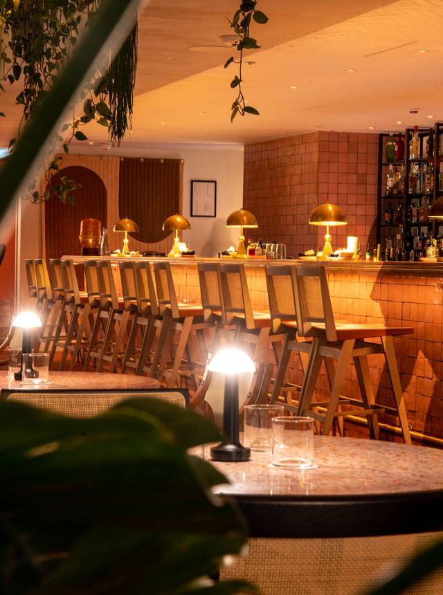 A long wooden bar featuring stools and decorative lamps, creating a warm and inviting atmosphere.