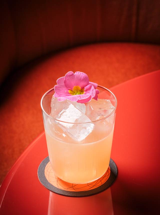 A refreshing cocktail with ice and a flower, elegantly placed on a vibrant red table.