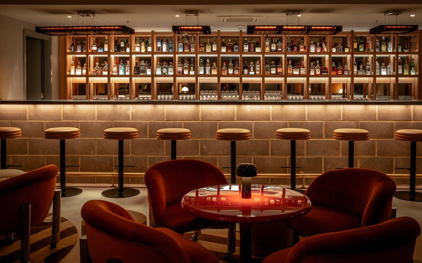 A vibrant bar featuring orange chairs illuminated by a striking red light, creating a lively atmosphere.