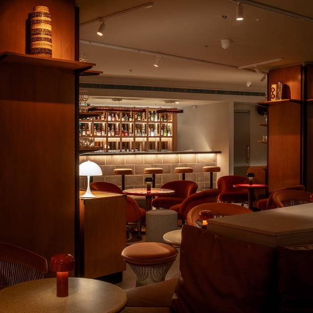 Intimate London bar area with a warm, moody atmosphere, red seating, and a well-stocked backlit bar.