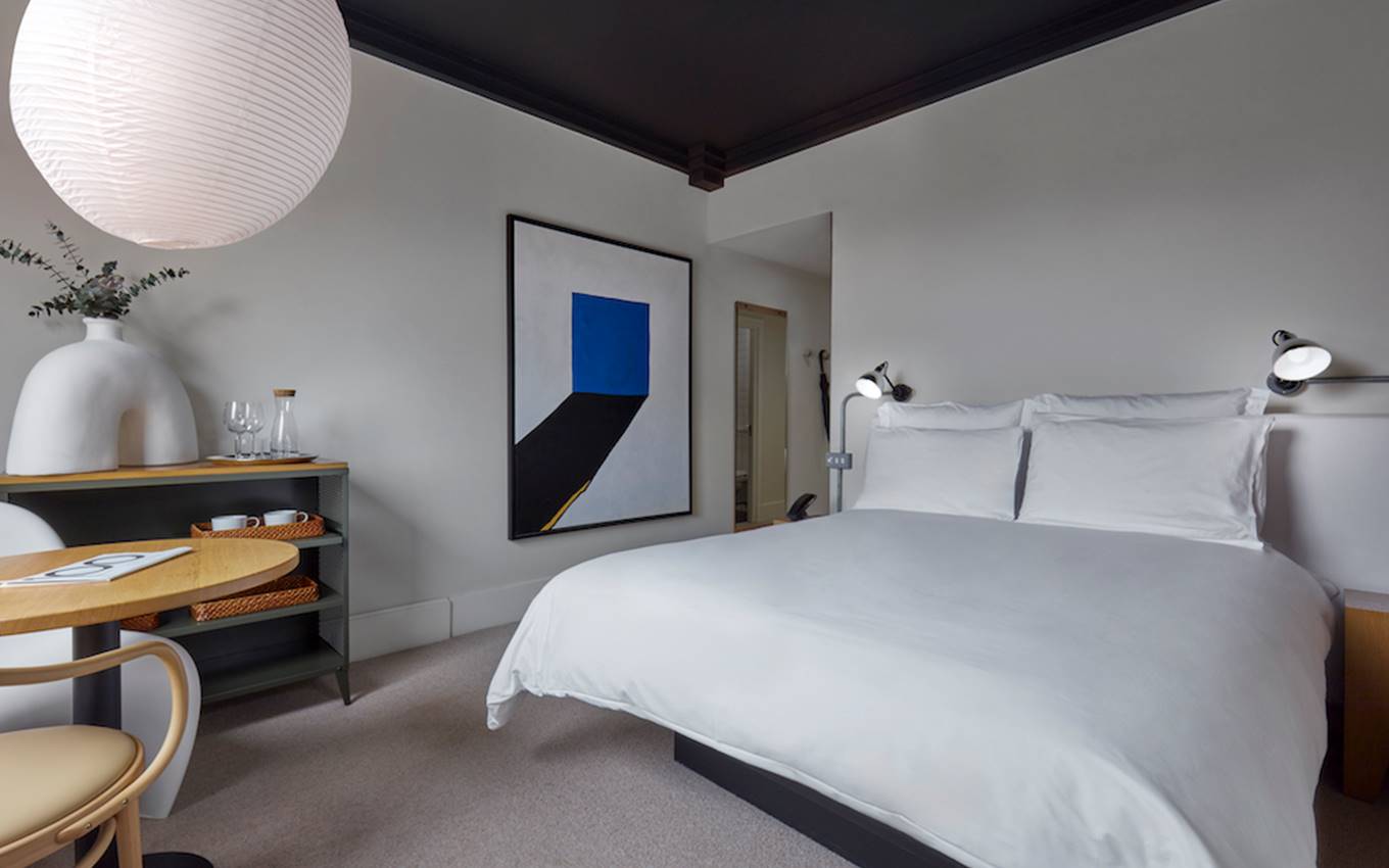 A modern and welcoming bedroom featuring a bed, a table, and a decorative painting on the wall.