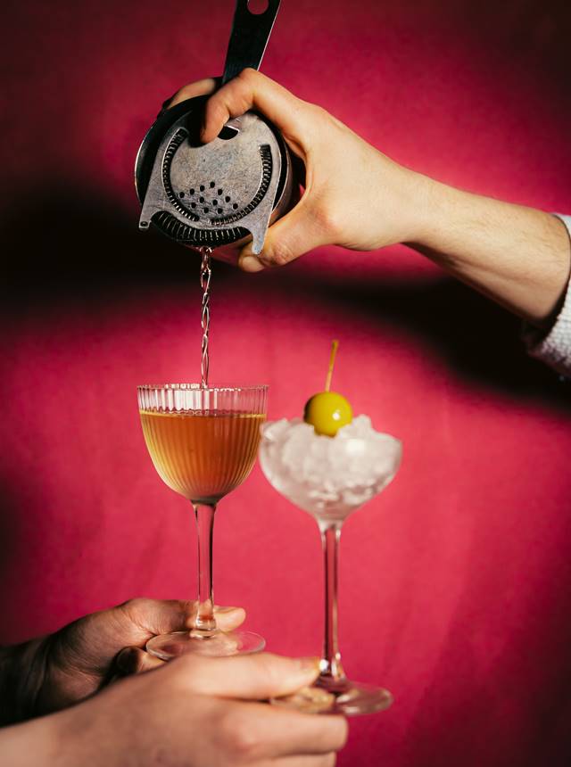 Two hands elegantly holding glasses filled with colourful drinks, showcasing a moment of celebration and togetherness.