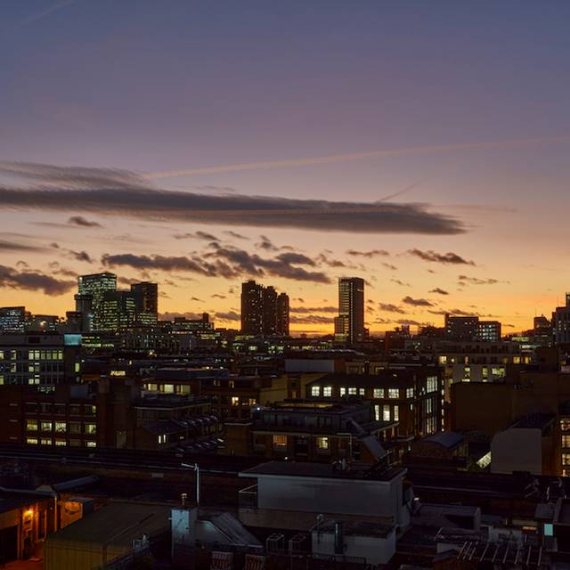 The sun sets over London city centre, casting a warm glow on the skyline and illuminating the iconic buildings.